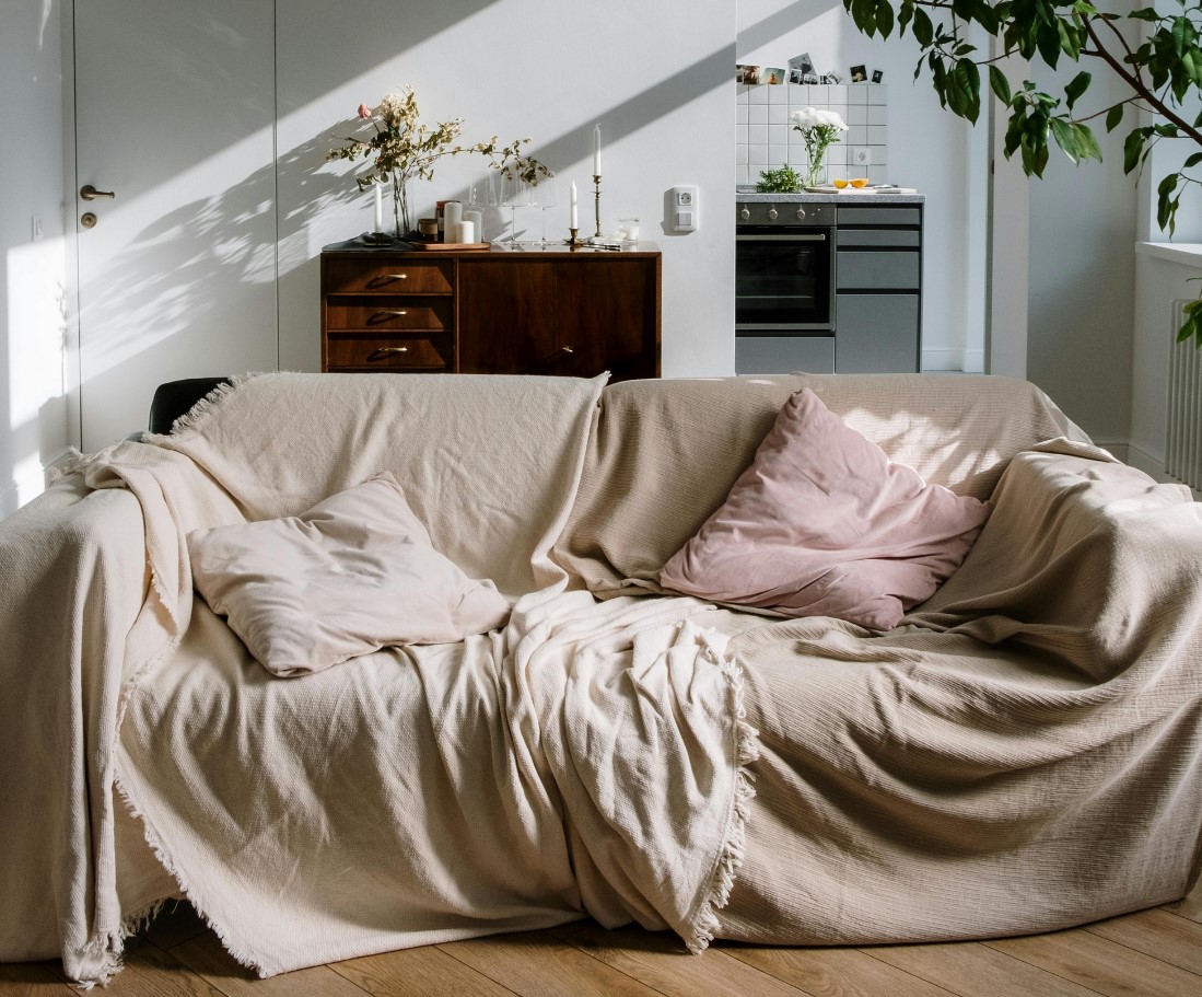 Couch with large beige sheets and cushions in a living room, during the day time