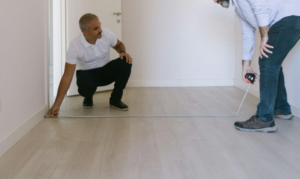 Two men measuring an empty small room, light colors