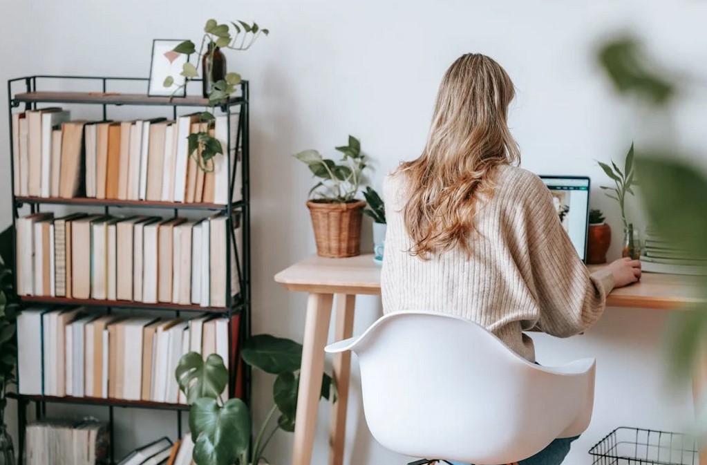 Woman sitting in a white chair in a room with a small book shelf library