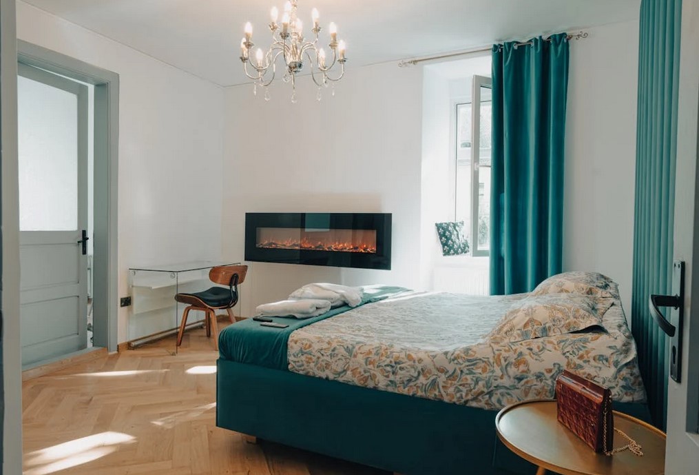 A hotel styled room with a built in fireplace in the wall, light colors with green accents