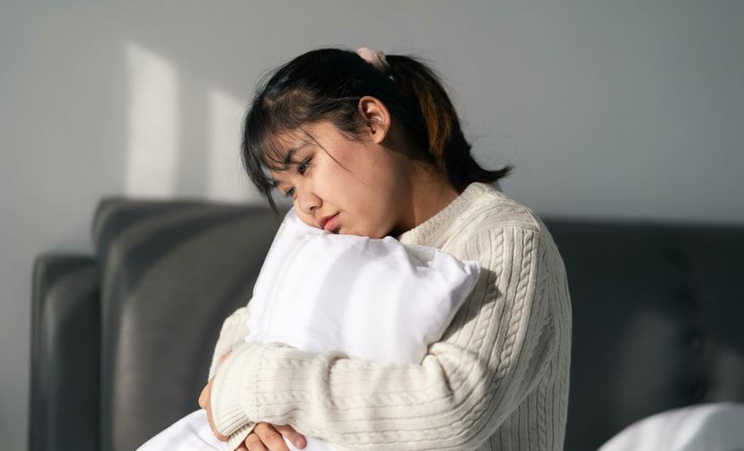 A young woman deep in thought hugging a white pilow