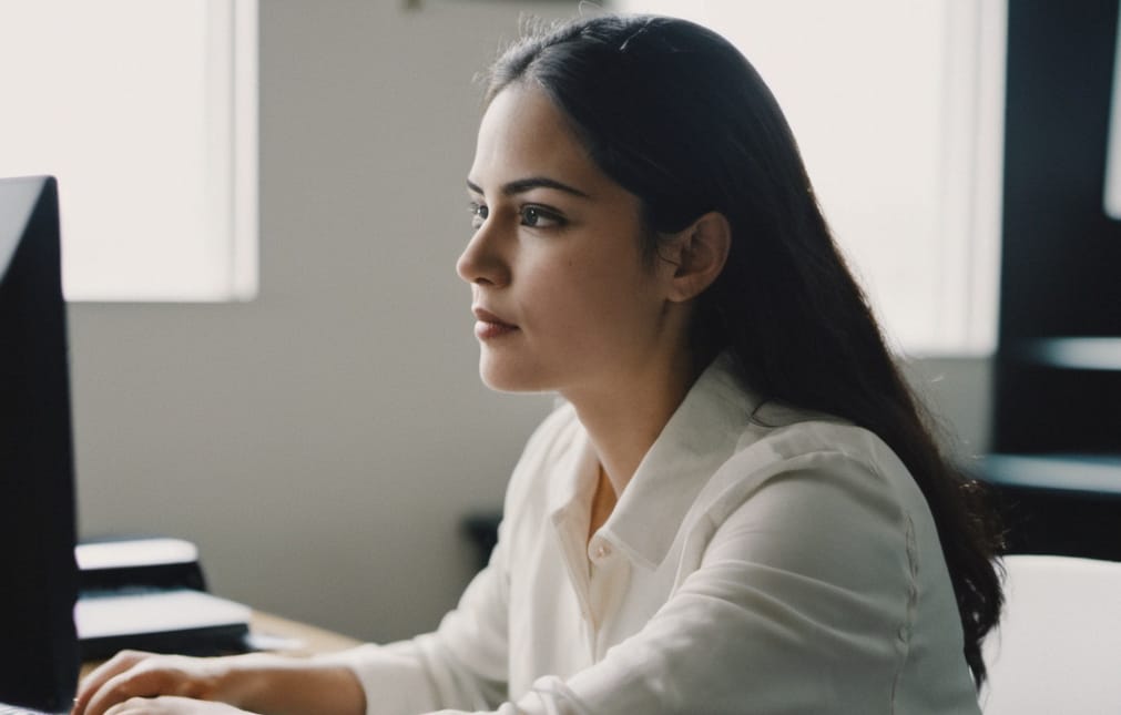 Woman with black hair and white shirt at her computer studying